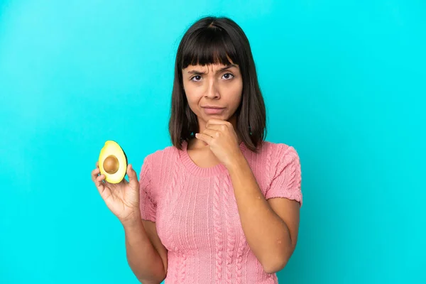 Young Mixed Race Woman Holding Avocado Isolated Blue Background Thinking — стоковое фото