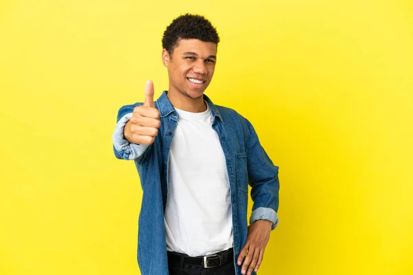 年轻的非洲裔美国人 有黄色背景 大拇指翘起 因为发生了一些好事 — 图库照片