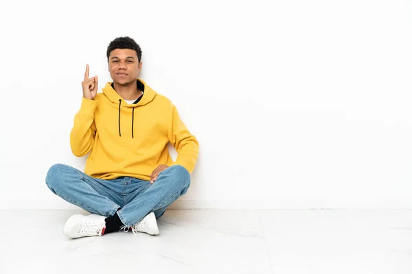 Mladý Afroameričan Sedí Podlaze Izolovaný Bílém Pozadí Ukazuje Ukazováčkem Skvělý — Stock fotografie