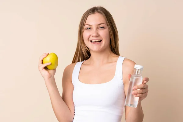 十代のウクライナ人の女の子は リンゴと水のボトルでベージュの背景に隔離されました — ストック写真
