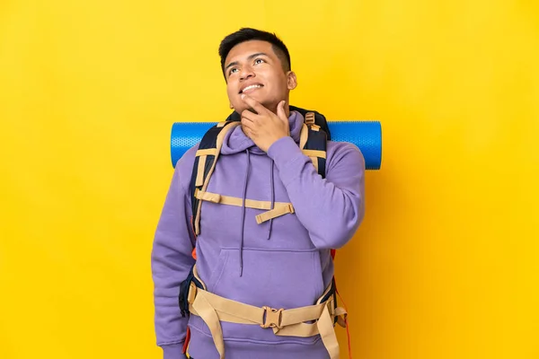 若い登山家の男は大きなバックパックを黄色の背景に上を見上げながら笑みを浮かべて隔離 — ストック写真
