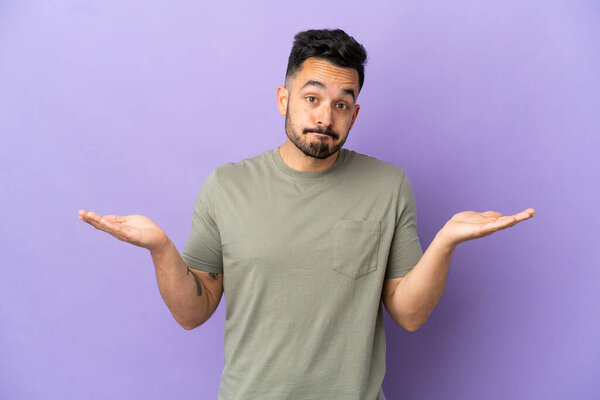 Young caucasian man isolated on purple background making doubts gesture