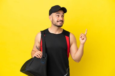 Sarı arka planda izole edilmiş spor çantalı beyaz bir adam harika bir fikre işaret ediyor.