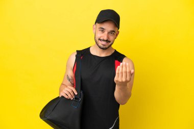 Spor çantalı beyaz bir genç, sarı arka planda izole edilmiş bir şekilde bizimle gelmesi için davet ediliyor. Gelmene sevindim.