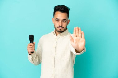 Beyaz tenli genç şarkıcı, mavi arka planda izole edilmiş bir şekilde duruyor.