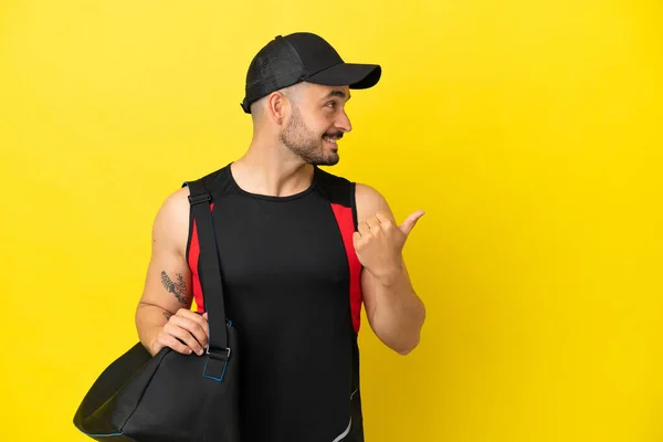 スポーツバッグと若いスポーツ白人男性は 製品を提示する側を指して黄色の背景に隔離された — ストック写真