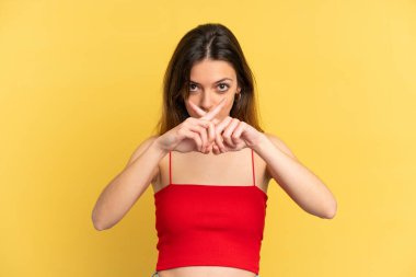 Sarı arka planda izole edilmiş genç beyaz kadın sessizlik işareti gösteriyor.