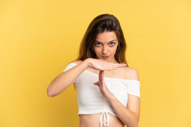 Sarı arka planda izole edilmiş genç beyaz bir kadın zaman aşımı hareketi yapıyor.