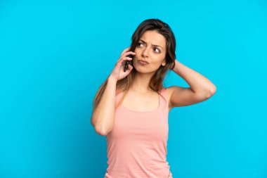 Mavi arka planda izole edilmiş cep telefonu kullanan beyaz bir kadın şüpheleri var.