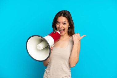 Mavi arka planda izole edilmiş genç beyaz kadın megafonla bağırıyor ve işaret ediyor.