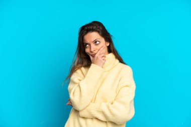 Kafkasyalı genç bir kadın mavi arka planda izole edilmiş. Şüpheleri var ve kafası karışmış bir yüz ifadesi var.