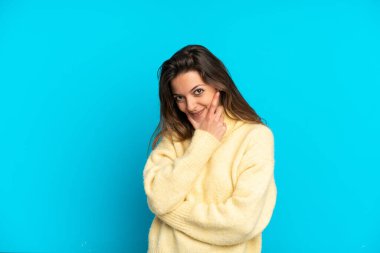 Mavi arka planda izole edilmiş genç beyaz kadın mutlu ve gülümsüyor.