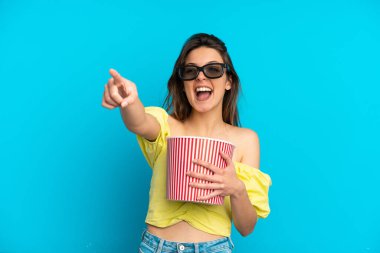 Mavi arka planda 3 boyutlu gözlüklü ve elinde koca bir kova patlamış mısırla dolaşan beyaz bir kadın.