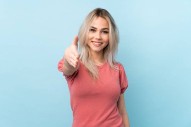 İzole edilmiş mavi arka planda genç kız iyi bir anlaşma için el sıkışıyor.