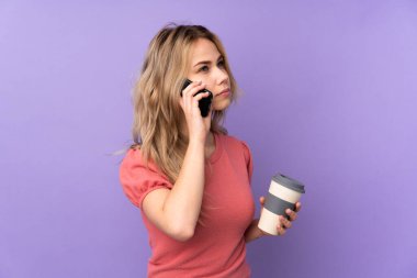 Mor arka planda izole edilmiş genç bir Rus kız elinde kahve ve cep telefonu var.