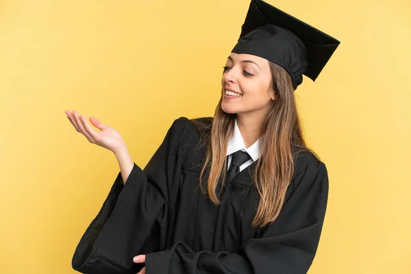 Junge Universitätsabsolventin Isoliert Auf Gelbem Hintergrund Die Hände Zur Seite — Stockfoto