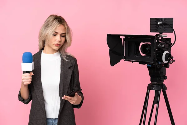记者妇女手持话筒 在孤立的粉色背景上报道新闻 手里拿着咖啡和手机 — 图库照片
