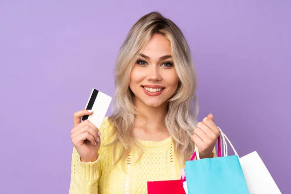 Tonåring Blond Flicka Över Isolerad Lila Bakgrund Innehav Shoppingväskor Och — Stockfoto