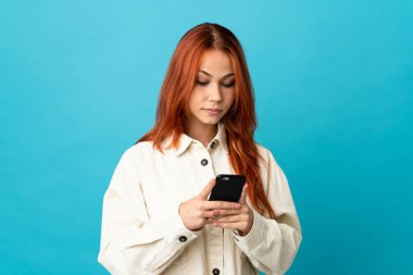 Genç Rus kız cep telefonu kullanarak mavi arka planda izole edilmiş.