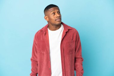 Genç latin adam mavi arka planda izole edilmiş bir şekilde bakarken bir fikir düşünüyor.