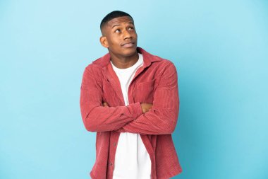 Genç latin adam mavi arka planda izole edilmiş gülümserken yukarı bakıyor