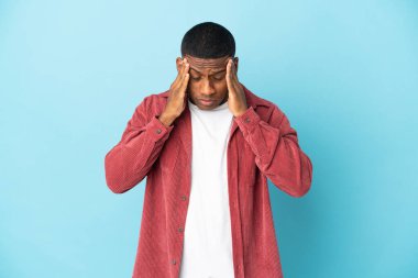 Mavi arka planda başağrısı olan genç Latin bir adam.