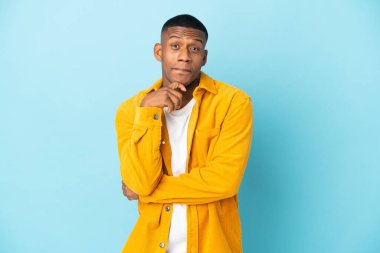 Genç Latin bir adam mavi arka planda izole edilmiş. Şüpheleri ve düşünceleri var.