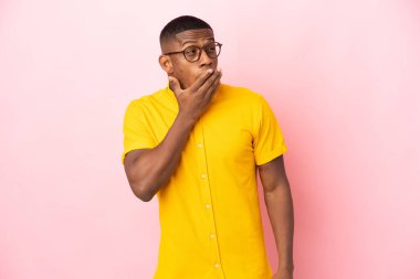 Pembe arka planda izole edilmiş genç bir latin adam esniyor ve ağzını eliyle kapatıyor.