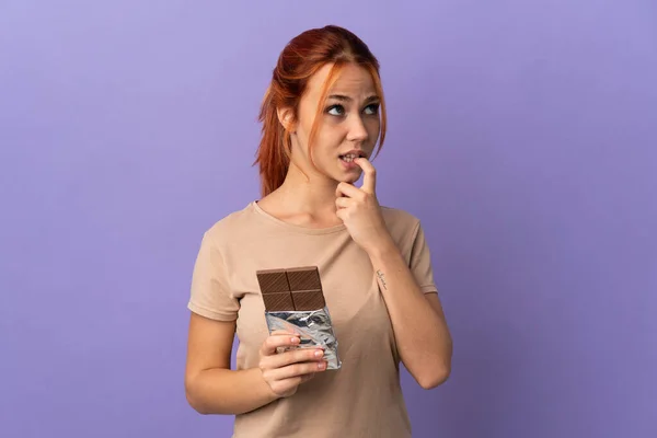 Teenager Ruské Dívka Izolované Fialovém Pozadí Čokoládovou Tabletu Mají Pochybnosti — Stock fotografie
