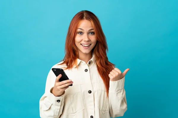 Tini Orosz Lány Elszigetelt Kék Háttér Segítségével Mobiltelefon Rámutatva Oldalsó — Stock Fotó