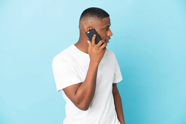 Fiatal Latin Férfi Elszigetelt Kék Háttér Miközben Egy Beszélgetést Mobiltelefon — Stock Fotó