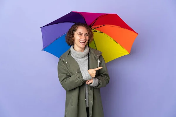 English Woman Holding Umbrella Isolated Purple Background Pointing Finger Side — 图库照片