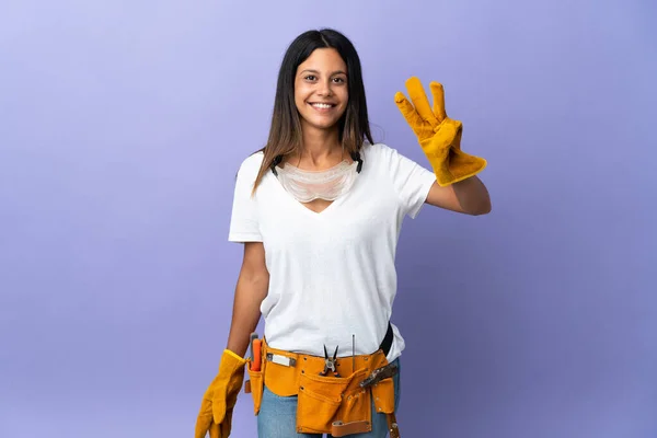 年轻的电工女人幸福地与紫色背景隔离 用手指数着三个 — 图库照片