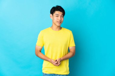 Genç Çinli adam mavi arka planda yalnız gülüyor.