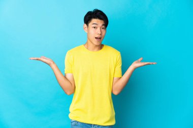 Young Chinese man isolated on blue background with shocked facial expression