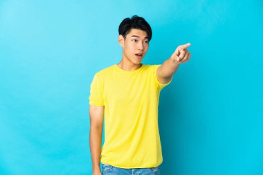 Young Chinese man isolated on blue background pointing away