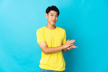 Young Chinese man isolated on blue background applauding