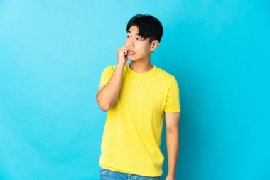 Young Chinese man isolated on blue background is a little bit nervous
