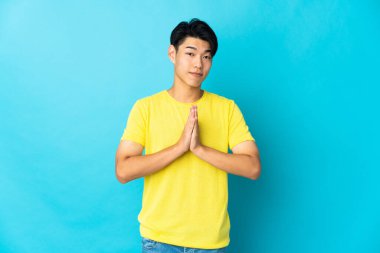 Mavi arka planda izole edilmiş genç bir Çinli avuç içlerini bir arada tutuyor. İnsan bir şey ister.