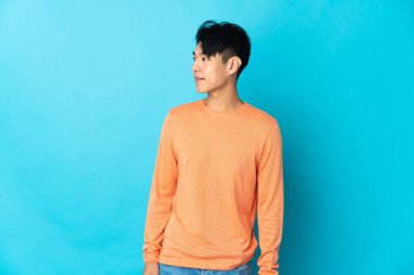 Young Chinese man isolated on blue background looking side