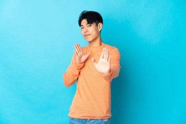 Young Chinese man isolated on blue background nervous stretching hands to the front