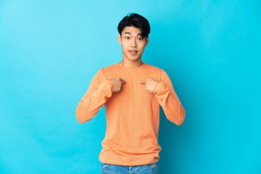 Genç Çinli bir adam mavi arka planda izole edilmiş ve yüzünde sürpriz bir ifade var.