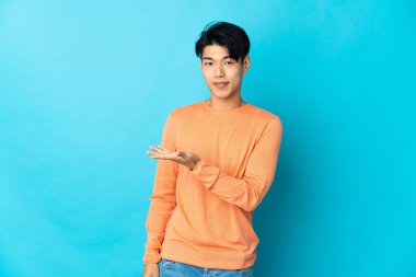 Young Chinese man isolated on blue background presenting an idea while looking smiling towards