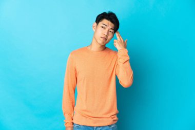Young Chinese man isolated on blue background with problems making suicide gesture