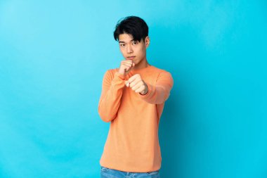 Young Chinese man isolated on blue background with fighting gesture