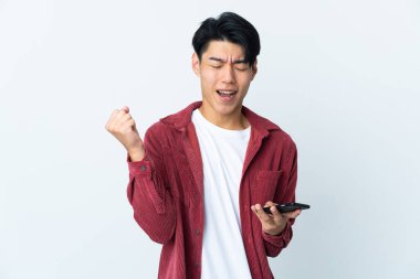 Genç Çinli adam beyaz arka planda cep telefonu kullanarak ve zafer jesti yaparak izole edildi.