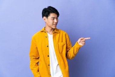 Mor arka planda izole edilmiş genç bir Çinli parmak göstererek bir ürün sunuyor.