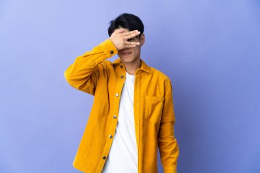 Mor arka planda izole edilmiş genç bir Çinli gözlerini elleriyle kapatıyor ve gülümsüyor.