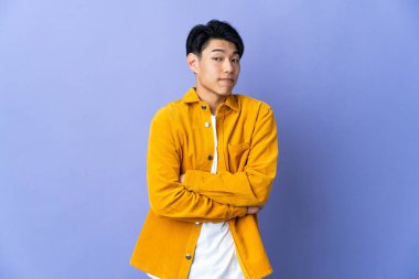 Young Chinese man isolated on purple background making doubts gesture while lifting the shoulders