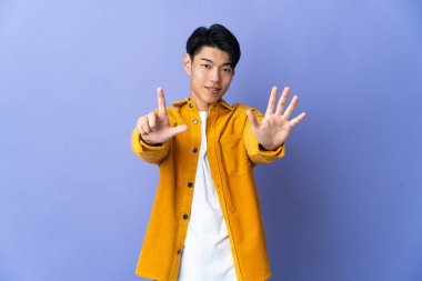Young Chinese man isolated on purple background counting seven with fingers